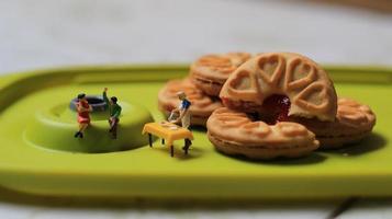 miniatura figuras do uma casal falando em uma verde jantar mesa perto uma chefe de cozinha cozinhando em uma fundo do uma bolo preenchidas com morango geléia. discussão conceito. foto