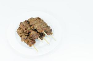 grelhado carne de porco com bambu bastão dentro branco prato em branco plano de fundo, tailandês estilizado grade carne de porco churrasco foto