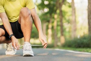 jovem atleta homem amarrar corrida sapatos dentro a parque ar livre, masculino corredor pronto para corrida em a estrada fora, ásia ginástica caminhando e exercício em trilha dentro manhã. bem estar e esporte conceitos foto