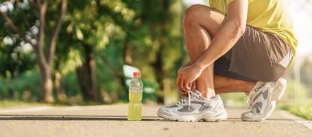 jovem atleta homem amarrar corrida sapatos com energia beber água, masculino corredor pronto para corrida fora, ásia ginástica caminhando e exercício dentro a parque manhã. bem-estar, bem estar e esporte conceitos foto