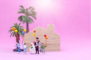 casal e família em miniatura com balões coloridos celebrando em um fundo rosa, conceito de casamento foto