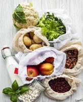 frutas e vegetais frescos em sacos de algodão ecológico na mesa da cozinha foto