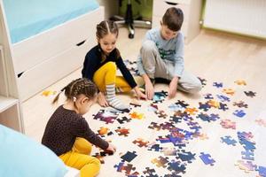 crianças conectando peças de quebra-cabeça em um quarto infantil no chão de casa. diversão em família atividade lazer. foto