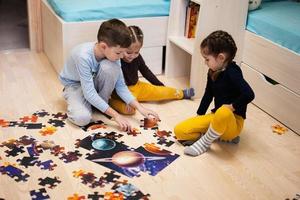 crianças conectando peças de quebra-cabeça em um quarto infantil no chão de casa. diversão em família atividade lazer. foto