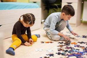 crianças conectando peças de quebra-cabeça em um quarto infantil no chão de casa. diversão em família atividade lazer. foto