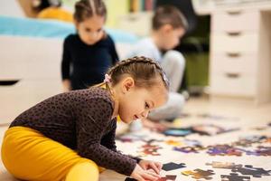 crianças conectando peças de quebra-cabeça em um quarto infantil no chão de casa. diversão em família atividade lazer. foto