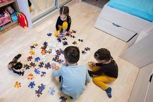 crianças conectando peças de quebra-cabeça em um quarto infantil no chão de casa. diversão em família atividade lazer. foto