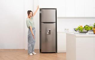 ásia mulher em pé Próximo para a geladeira dentro a cozinha foto