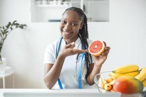 retrato de jovem nutricionista feminina sorridente na sala de consulta. mesa de nutricionista com frutas saudáveis, suco e fita métrica. nutricionista trabalhando no plano de dieta. foto