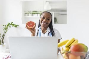 retrato de jovem nutricionista feminina sorridente na sala de consulta. mesa de nutricionista com frutas saudáveis, suco e fita métrica. nutricionista trabalhando no plano de dieta. foto
