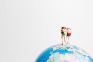 pessoas em miniatura em um globo com um fundo branco, conceito de viagens foto