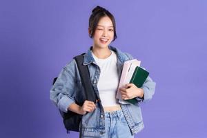retrato do uma lindo ásia estudante vestindo uma mochila em uma roxa fundo foto