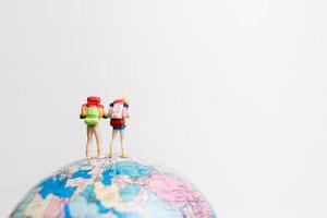 pessoas em miniatura em um globo com um fundo branco, conceito de viagens foto