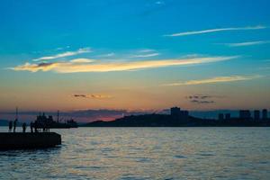 vista do mar com a silhueta de pessoas em um píer com o pôr do sol nublado colorido em Vladivostok, Rússia foto