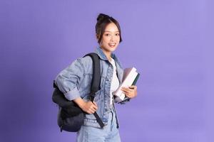 retrato do uma lindo ásia estudante vestindo uma mochila em uma roxa fundo foto