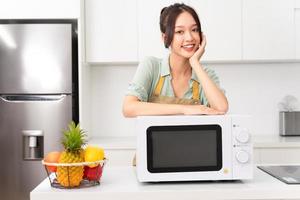 ásia menina em pé Próximo para a microondas dentro dela cozinha foto