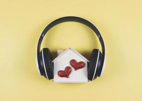 plano deitar do de madeira modelo casa com dois vermelho brilhar corações coberto com fones de ouvido isolado em amarelo fundo. música ou podcast, casa do amor, dia dos namorados. foto