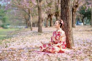 jovem senhora dentro tradicional quimono vestir práticas meditação às cereja Flor árvore. emoção sorrir foto