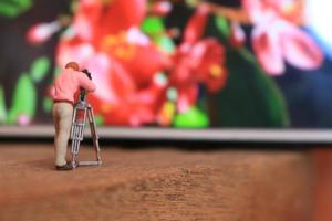 uma miniatura figura do uma cinegrafista filmando flores em uma célula telefone. foto