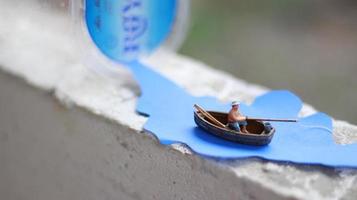 uma miniatura figura do uma pescador pescaria dentro uma rio visualizado em azul papel recortes. foto