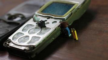 miniatura figura do uma técnico reparação a velho quebrado célula telefone. trabalhando técnico conceito. foto