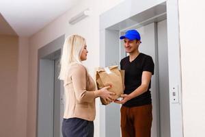 sorridente jovem mulher recebendo mercearias a partir de Entrega homem às apartamento foto