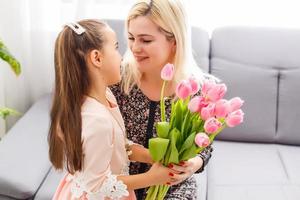 feliz mãe dia. criança filha parabeniza mãe e dá dela flores tulipas. mãe e menina sorridente e abraçando. família feriado e união. foto