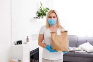 jovem mulher vestindo médico mascarar recebendo parcela a partir de Entrega dentro de casa. prevenção do vírus espalhar foto