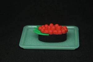 japonês Comida Sushi pequeno borracha brinquedo miniatura estacionário com único fofa forma. gunkan Sushi com salmão peixe ovos caviar em topo e nori embrulho por aí isto isolado em Sombrio Preto fundo. foto