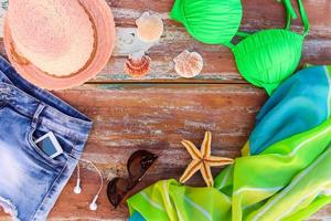 verão mulheres roupas e acessórios chapéu, tomando banho terno, jeans shorts, páreo, oculos de sol, Móvel telefone, fones de ouvido, cartuchos. topo visualizar. foto