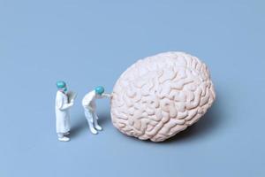 médicos em miniatura verificando e analisando um cérebro em busca de sinais da doença de Alzheimer e demência, ciência e conceito de medicina foto