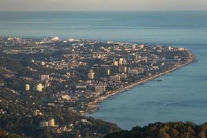 vista aérea de montanhas e cidade distante ao lado de corpo d'água em sochi, rússia foto