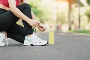 jovem atleta mulher amarrar corrida sapatos com energia beber água, fêmea corredor pronto para corrida fora, ásia ginástica caminhando e exercício dentro a parque manhã. bem-estar, bem estar e esporte conceitos foto