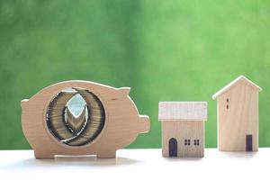pilha de moedas em um cofrinho de madeira com casas modelo em um fundo verde natural foto
