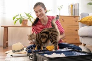 mochileiro viagem do jornada, ásia jovem mulher jogando com dela gato, animal enquanto Verifica lista, embalagem ou preparar roupas para dentro bagagem, viagem caso para viagem viagem. viagem do viajante, feriado período de férias. foto