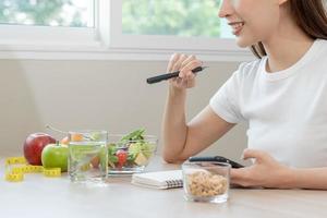 dieta, dieta mão do ásia jovem mulher trabalhando, escrever dieta plano certo nutrição com comer fresco legumes salada é Comida para Boa saúde não comer lixo Comida. nutricionista fêmea, peso perda do saudável. foto