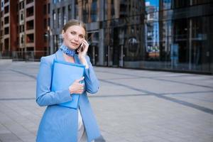 o negócio mulher dentro azul falando em a telefone com uma pasta dentro dela mão foto