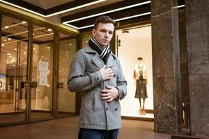 lindo modelo jovem cara dentro cinzento casaco posando em cidade rua durante dia. foto