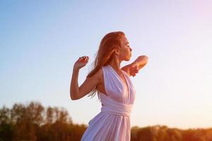 lindo delgado mulher dentro uma branco vestir de a mar às pôr do sol foto