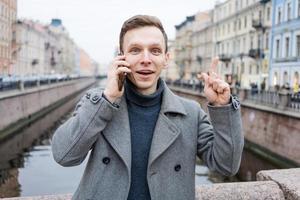 emocional jovem homem usando Móvel telefone, vestindo a elegante cinzento casaco, carrinhos foto