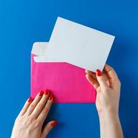 envelope rosa com um cartão em branco nas mãos sobre um fundo azul. foto