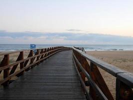 agradável de madeira ponte sobre a areia em a de praia foto