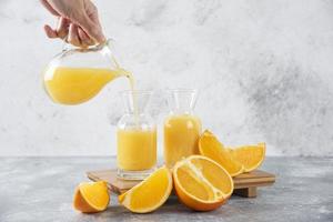 mão derramando suco de laranja fresco em um fundo de pedra foto
