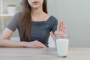 alergia ásia jovem mulher, menina mão dentro negar, não ou empurrar Fora para evitar para beber leite às lar, infeliz e mau estômago dor. lactose intolerância e laticínios comida, saúde problema, barriga Sofra conceito. foto