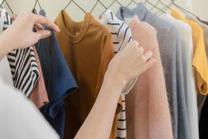 escolha do roupas, nada para vestem ásia jovem mulher, menina mão dentro escolhendo vestir, equipamento em cabide dentro guarda roupa dentro quarto armário de roupa às lar. decidir o que para colocar em que um. foto