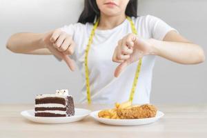 dieta, dieta pouco saudável ásia jovem mulher, menina mão dentro negar, rejeitando chocolate bolo ou doce gosto e frito frango, francês fritas ou lixo Comida. nutricionista do saudável, nutrição do peso perda. foto