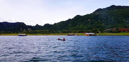 grandes rabo barco em rio com muitos casa ou recorrer, verde montanha, azul céu e nuvens às Srinakarin lago kanchanaburi, tailândia. lindo panorama Visão do natural, natureza papel de parede e vida em wate foto