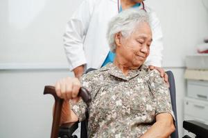 médico Socorro ásia idosos incapacidade mulher paciente segurando caminhando bastão dentro enrugado mão às hospital. foto