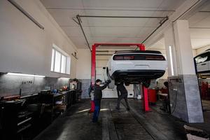 dois mecânicos na estação de reparo de serviço trabalhando com muscle car no elevador. foto