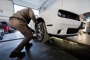 mecânico na estação de reparação de serviço trabalhando com muscle car. inspeciona a parte móvel da roda. foto